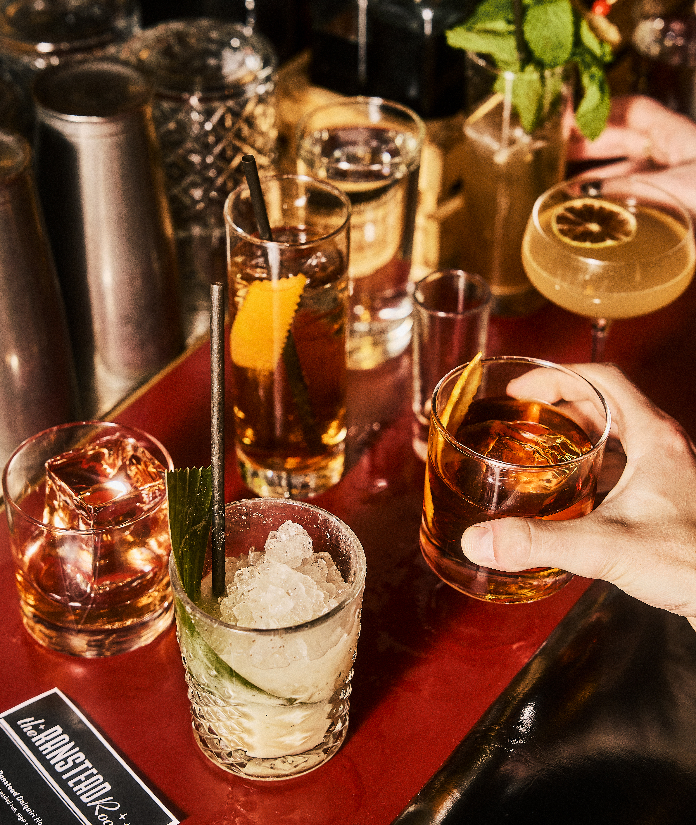 Assorted cocktails on a red bar table including whiskey drinks with ice and garnished beverages with straws
