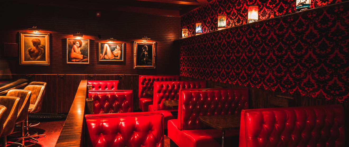 Luxurious lounge interior with red tufted leather seating, dark wood paneling, ornate wallpaper, and illuminated artwork
